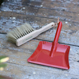Glückskäfer red metal dust pan and dust brush placed on a wooden surface.