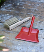 Glückskäfer red metal dust pan and dust brush placed on a wooden surface.