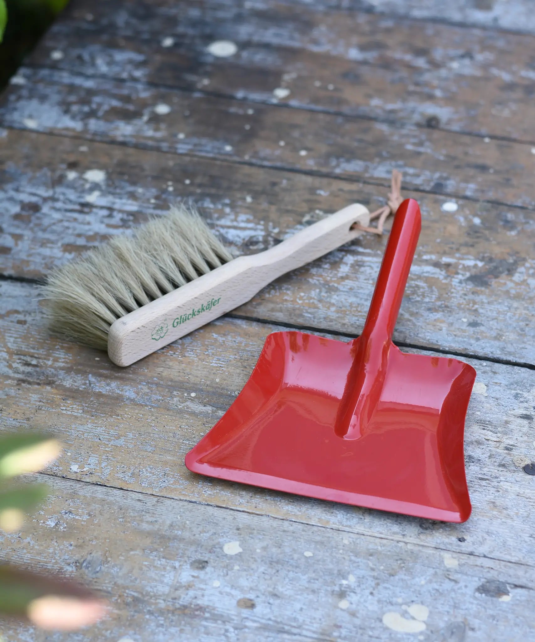 Glückskäfer red metal dust pan and dust brush placed on a wooden surface.