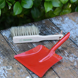 Glückskäfer red metal dust pan and dust brush placed on a wooden surface.