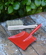 Glückskäfer red metal dust pan and dust brush placed on a wooden surface.