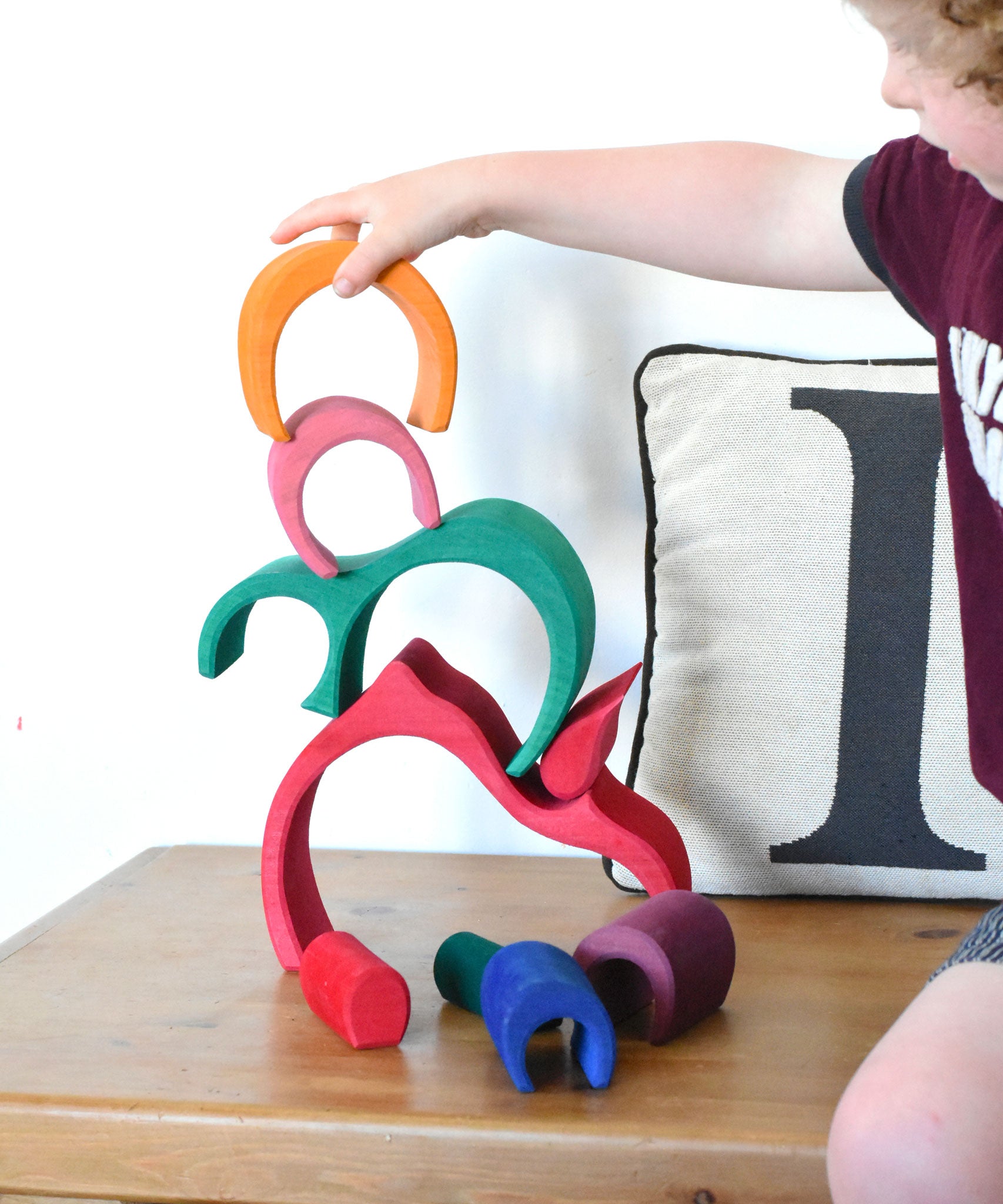 A child stacking the pieces from the Glückskäfer Gable House wooden toy set on top of each other. 