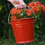 A close up of the Glückskäfer Red Metal Bucket in a child's hand.