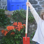 A child holding up the Glückskäfer Red Metal Spade by the wooden handle. 