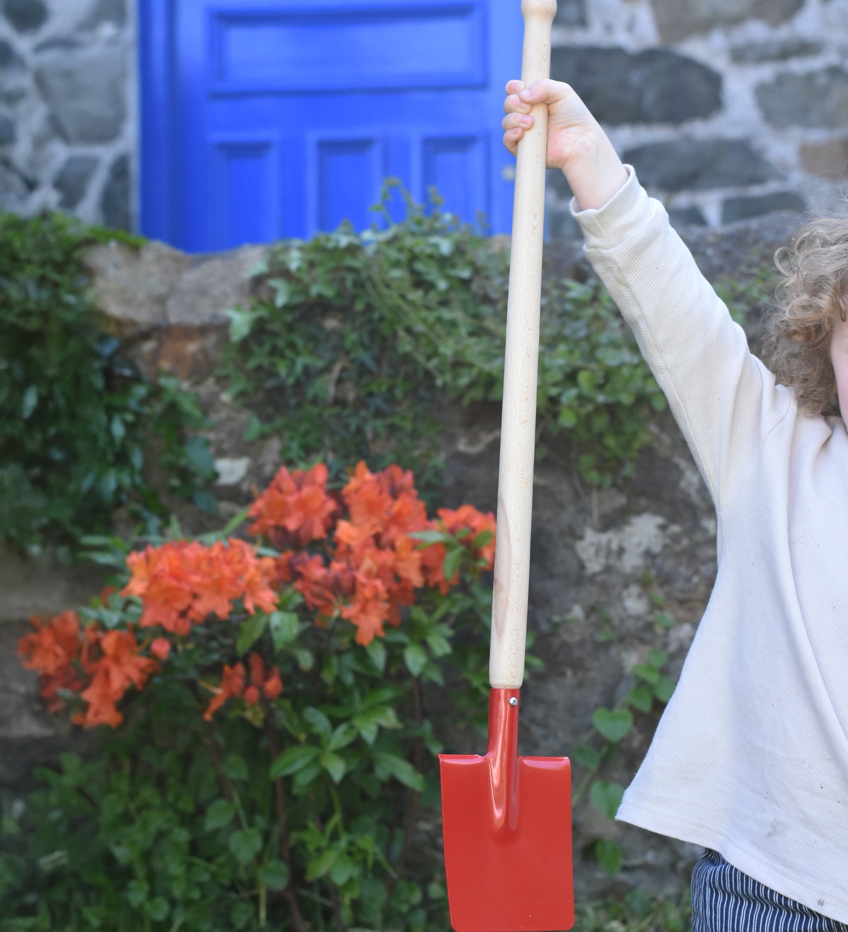 A child holding up the Glückskäfer Red Metal Spade by the wooden handle. 
