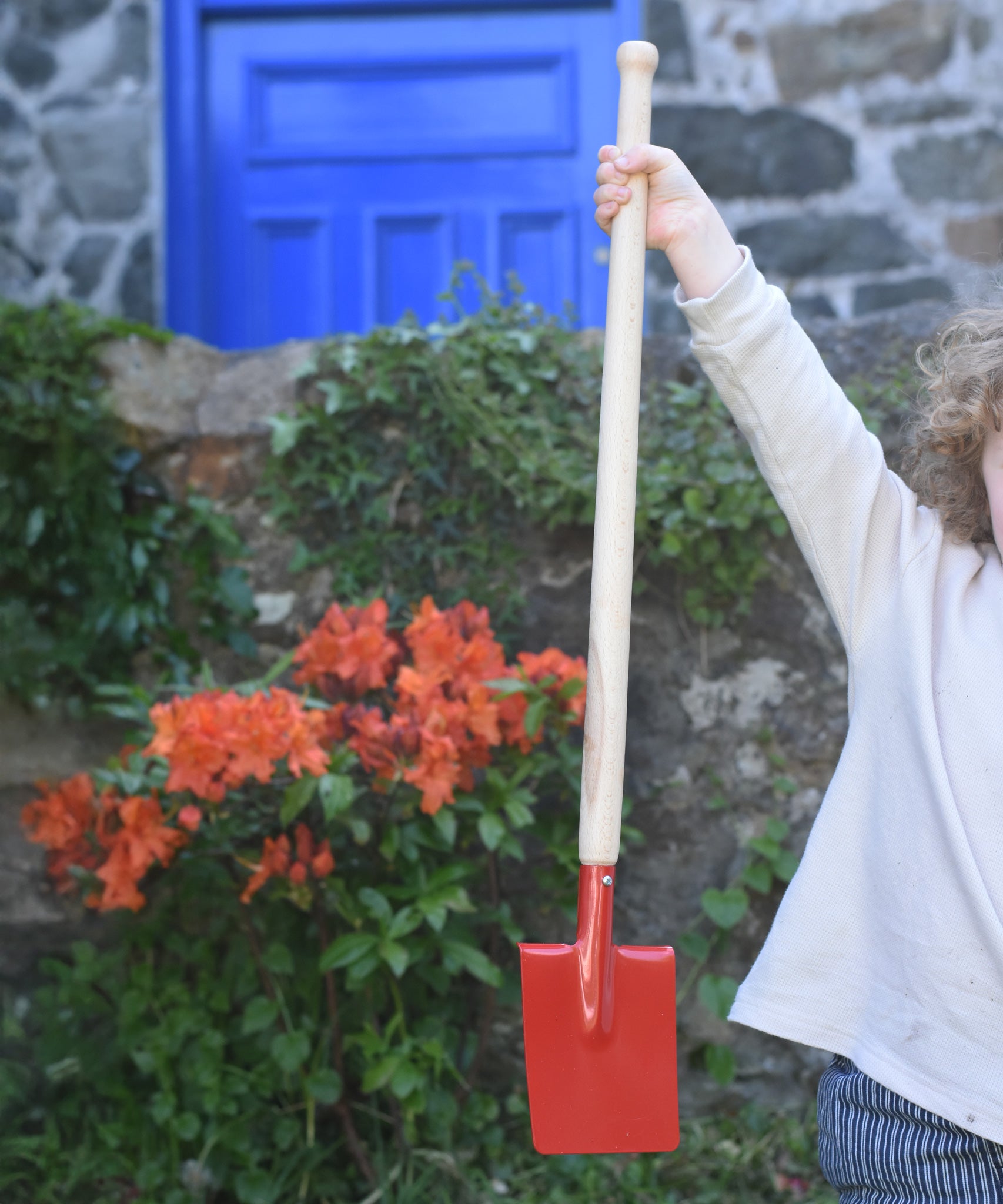 A child holding up the Glückskäfer Red Metal Spade by the wooden handle. 