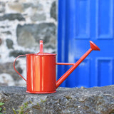 A Glückskäfer Red 1L Metal Watering placed on a stone wall outdoors.