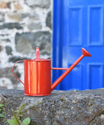 A Glückskäfer Red 1L Metal Watering placed on a stone wall outdoors.