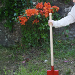 A child placing the Glückskäfer Red Metal Spade into a grassy surface on the ground.
