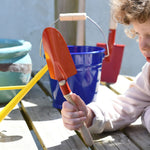 A child holding up a Glückskäfer Round Metal Red Shovel. 