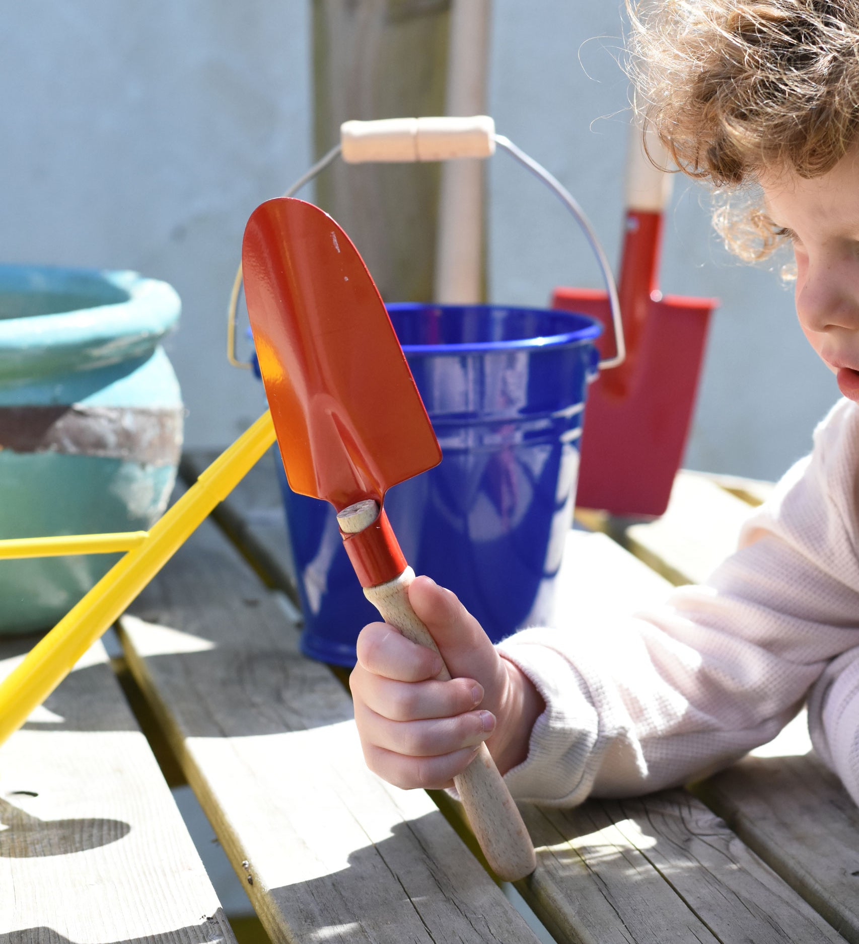 A child holding up a Glückskäfer Round Metal Red Shovel. 