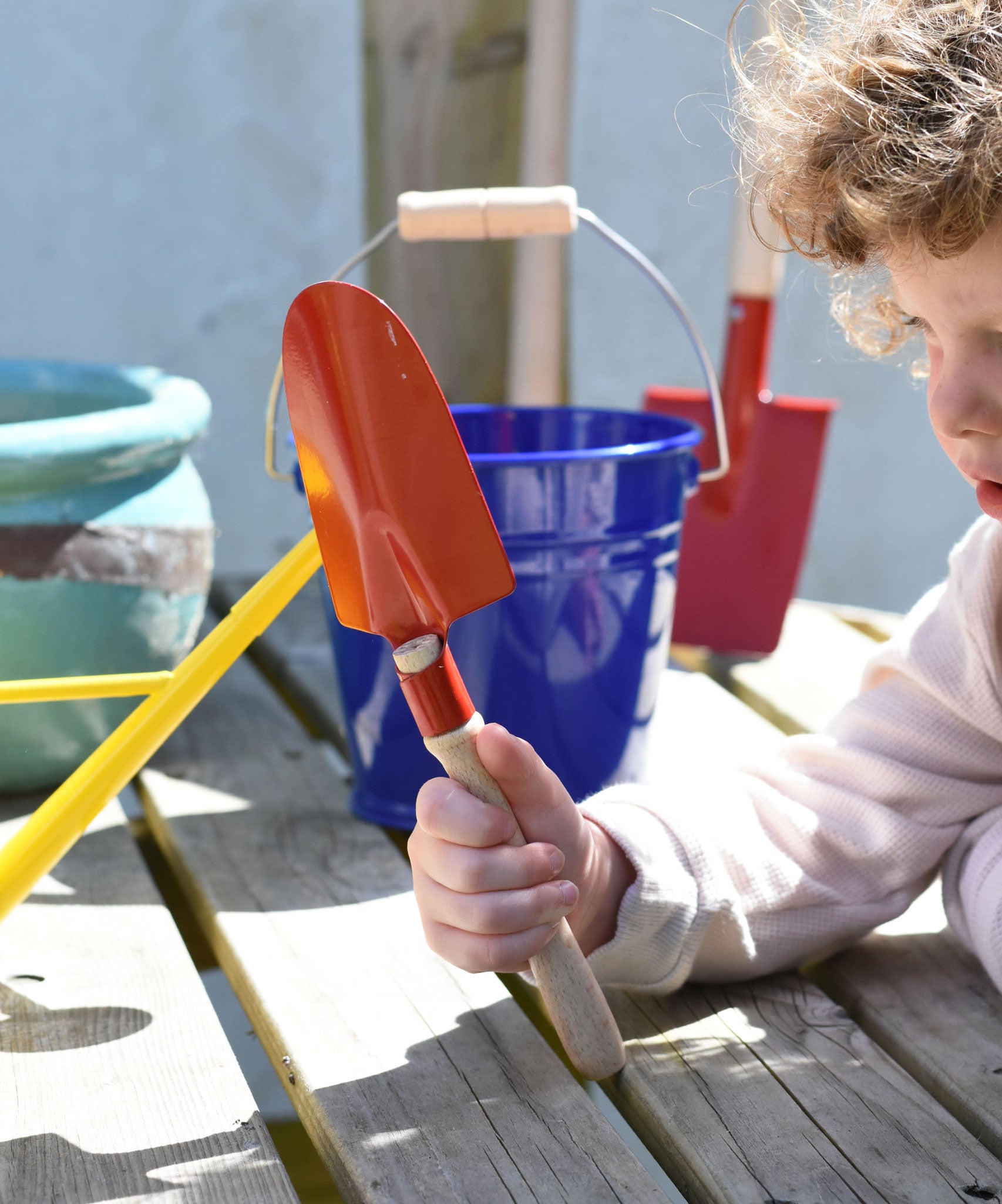 A child holding up a Glückskäfer Round Metal Red Shovel. 