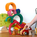 A child playing with a red Lanka Kade push along car with a Glückskäfer Gable House wooden stacking toy, stacked up in the background. 