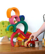 A child playing with a red Lanka Kade push along car with a Glückskäfer Gable House wooden stacking toy, stacked up in the background. 