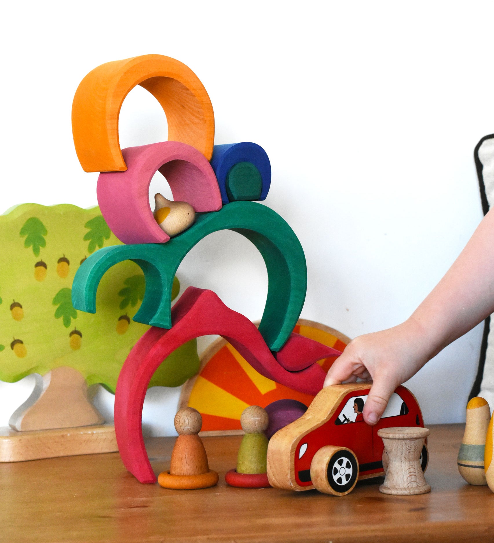 A child playing with a red Lanka Kade push along car with a Glückskäfer Gable House wooden stacking toy, stacked up in the background. 
