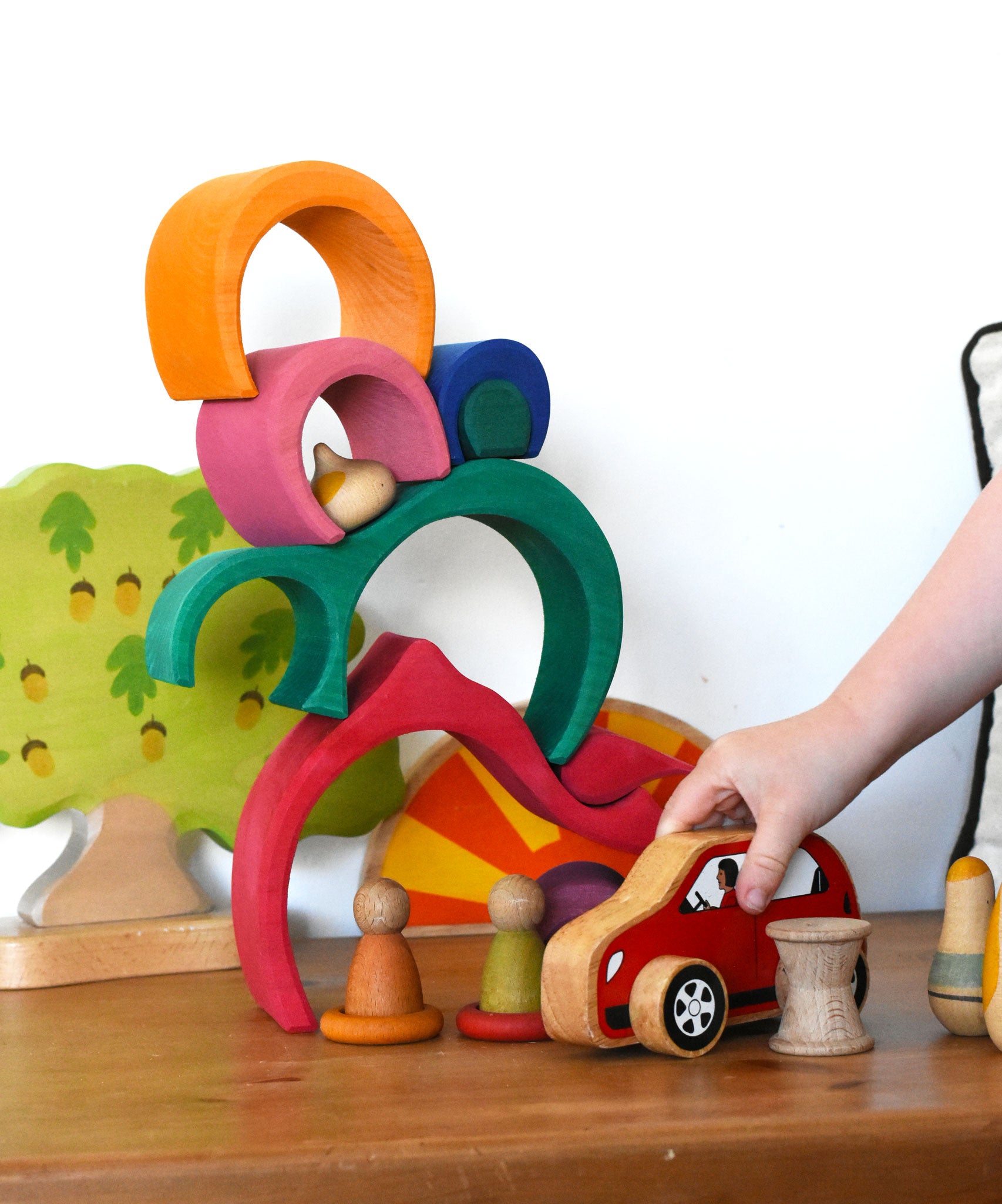 A child playing with a red Lanka Kade push along car with a Glückskäfer Gable House wooden stacking toy, stacked up in the background. 