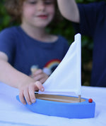Child playing with the Glückskäfer wooden sailing ship in blue.
