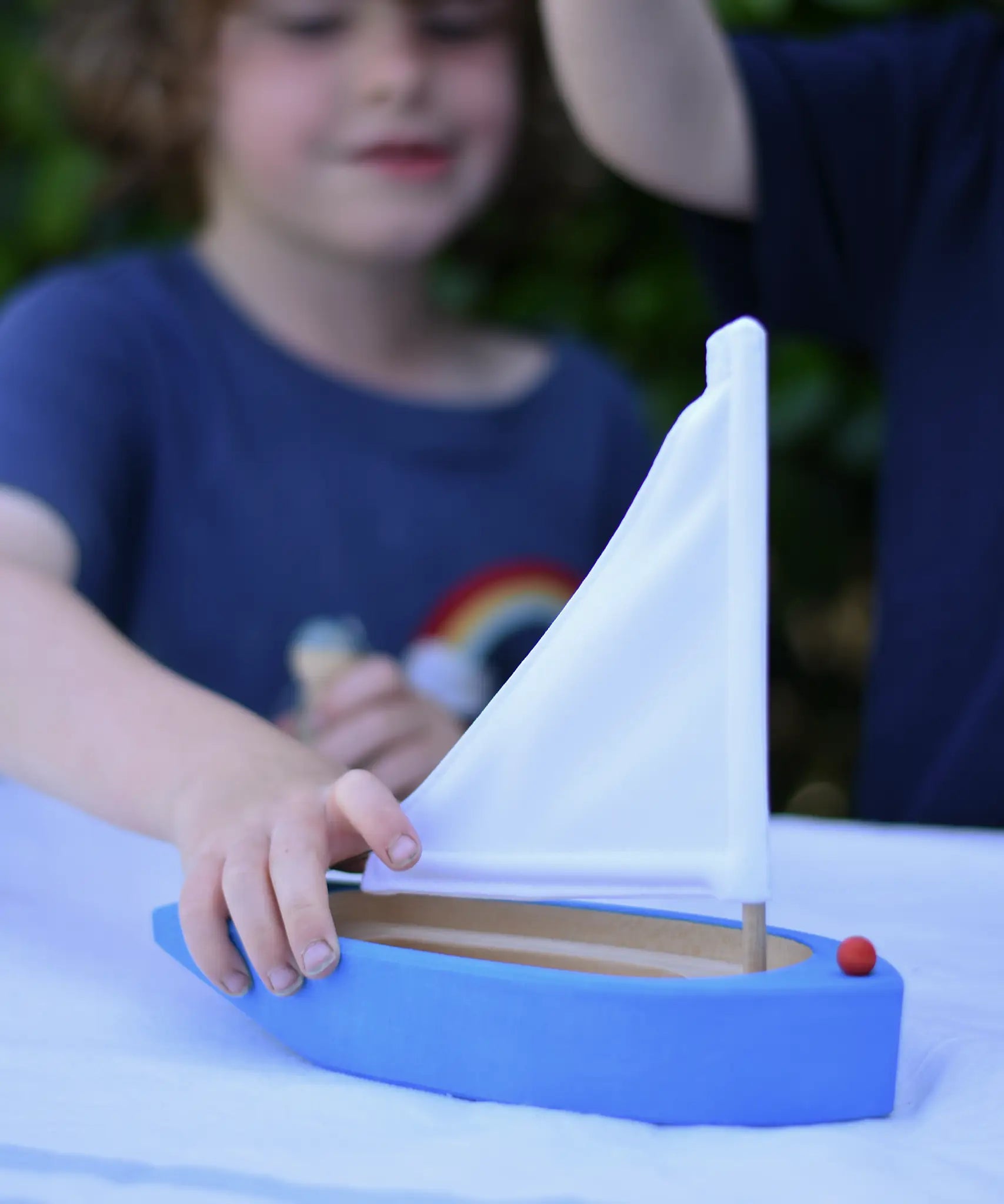 Child playing with the Glückskäfer wooden sailing ship in blue.