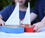 Children playing with the Glückskäfer wooden sailing ships, one blue and one red.  