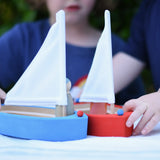 Children playing with the Glückskäfer wooden sailing ships, one blue and one red.  