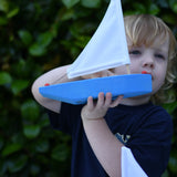 Child holding up the Glückskäfer wooden sailing ship in blue. 
