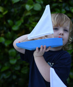 Child holding up the Glückskäfer wooden sailing ship in blue. 