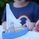 Glückskäfer wooden sailing ship in blue with a Grapat Nin placed inside. Child pushing the boat along.