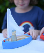Glückskäfer wooden sailing ship in blue with a Grapat Nin placed inside. Child pushing the boat along.