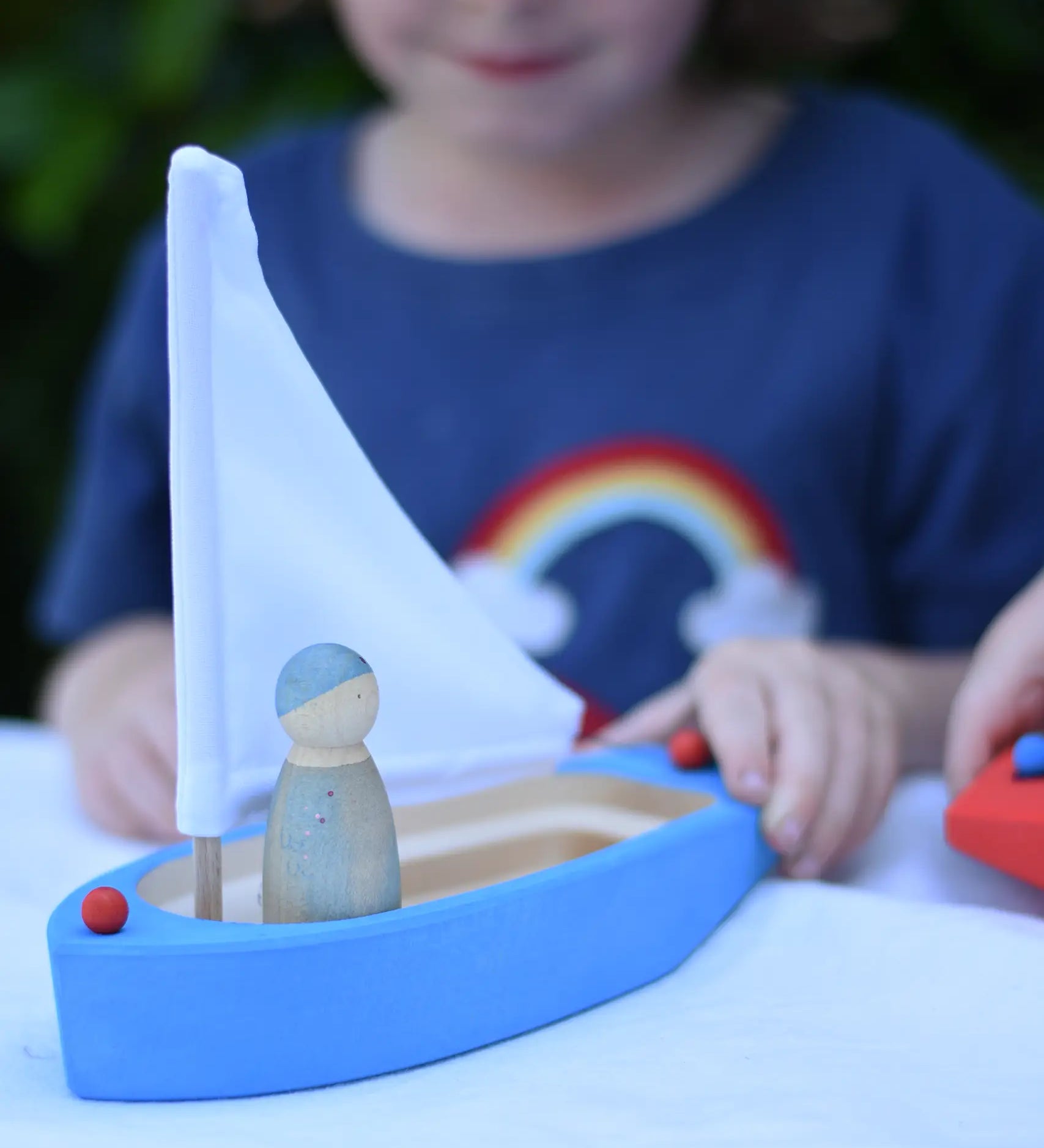 Glückskäfer wooden sailing ship in blue with a Grapat Nin placed inside. Child pushing the boat along.