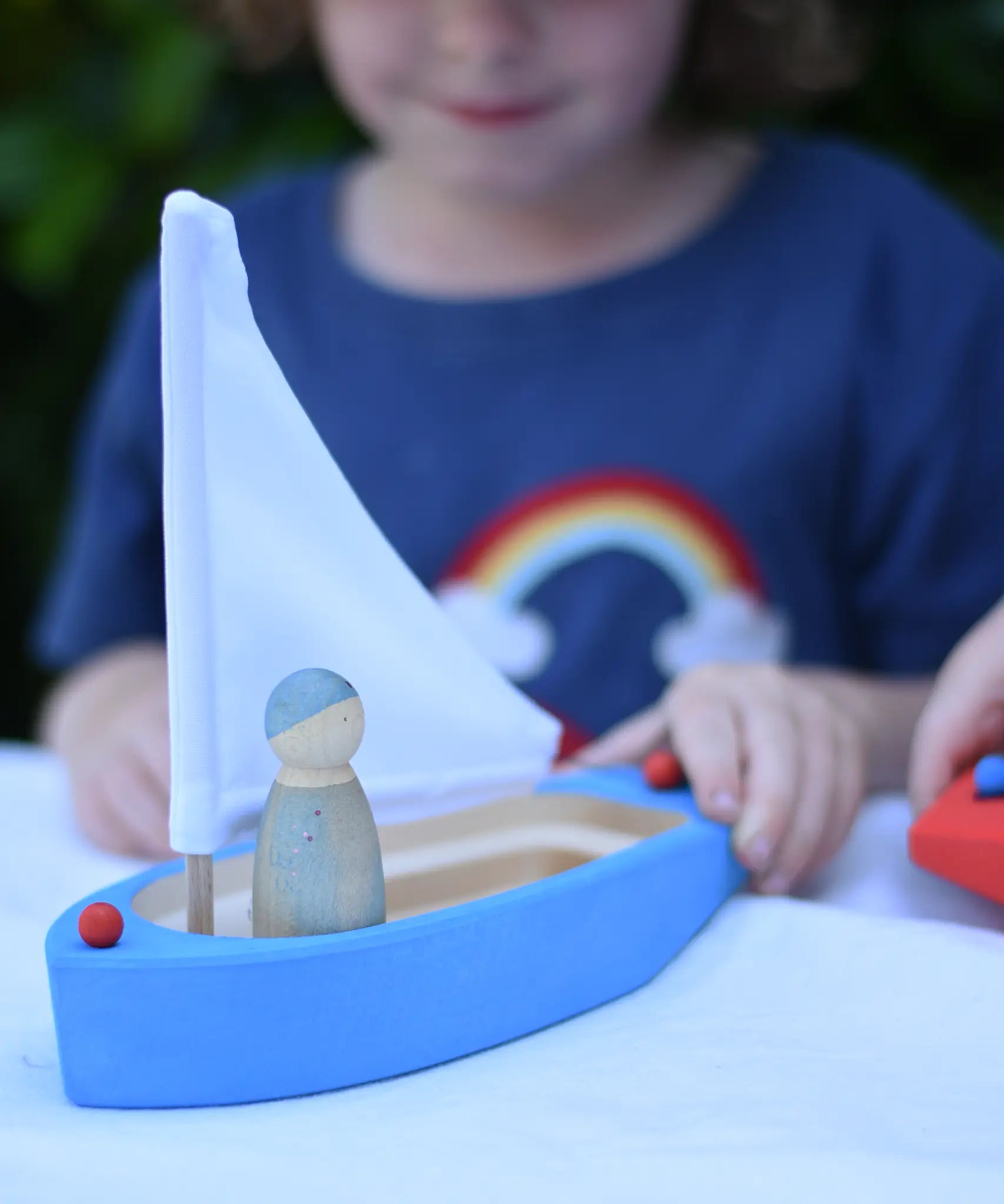 Glückskäfer wooden sailing ship in blue with a Grapat Nin placed inside. Child pushing the boat along.