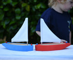 Two Glückskäfer wooden sailing ships in blue and red placed next to each other on a table.  