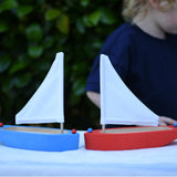 Two Glückskäfer wooden sailing ships in blue and red placed next to each other on a table.  