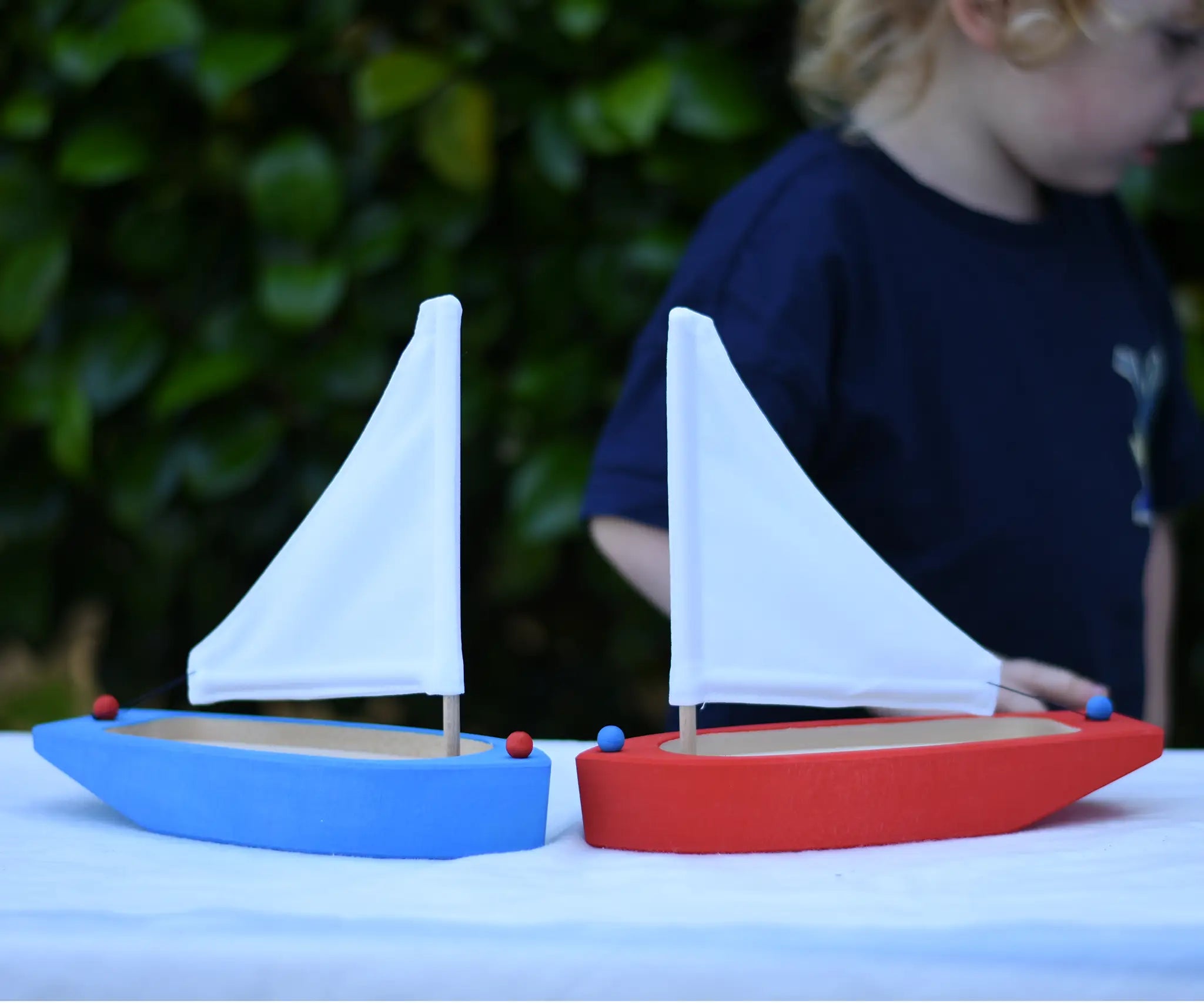 Two Glückskäfer wooden sailing ships in blue and red placed next to each other on a table.  