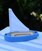 Glückskäfer wooden sailing ship in blue placed on a table outdoors.
