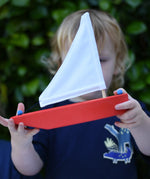 Child holding the Glückskäfer wooden sailing ship in red.
