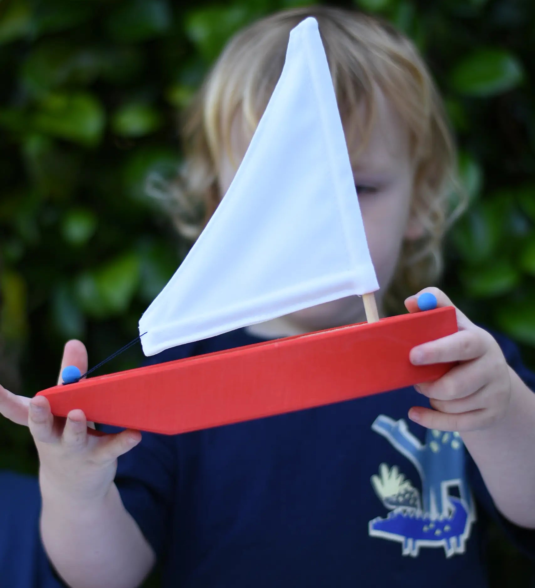 Child holding the Glückskäfer wooden sailing ship in red.