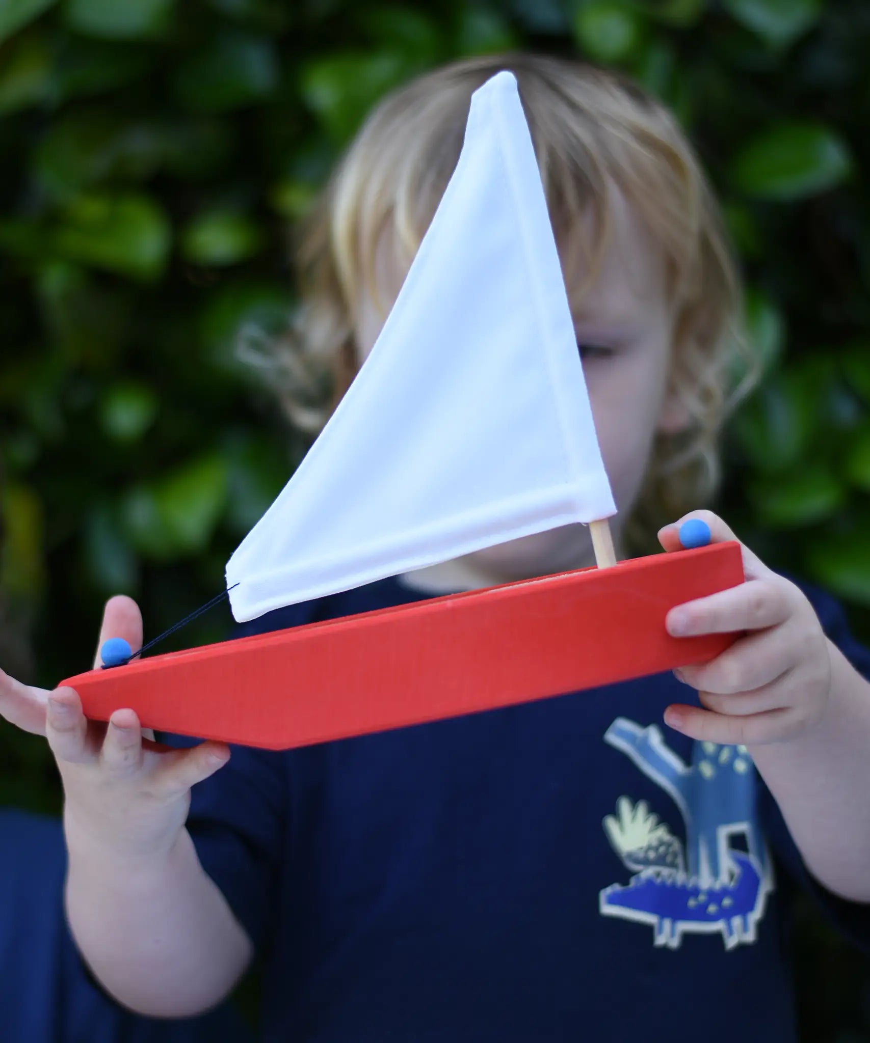 Child holding the Glückskäfer wooden sailing ship in red.