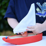 Child placing a Grapat Nin into the  Glückskäfer wooden sailing ship in red.