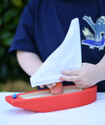 Child placing a Grapat Nin into the  Glückskäfer wooden sailing ship in red.