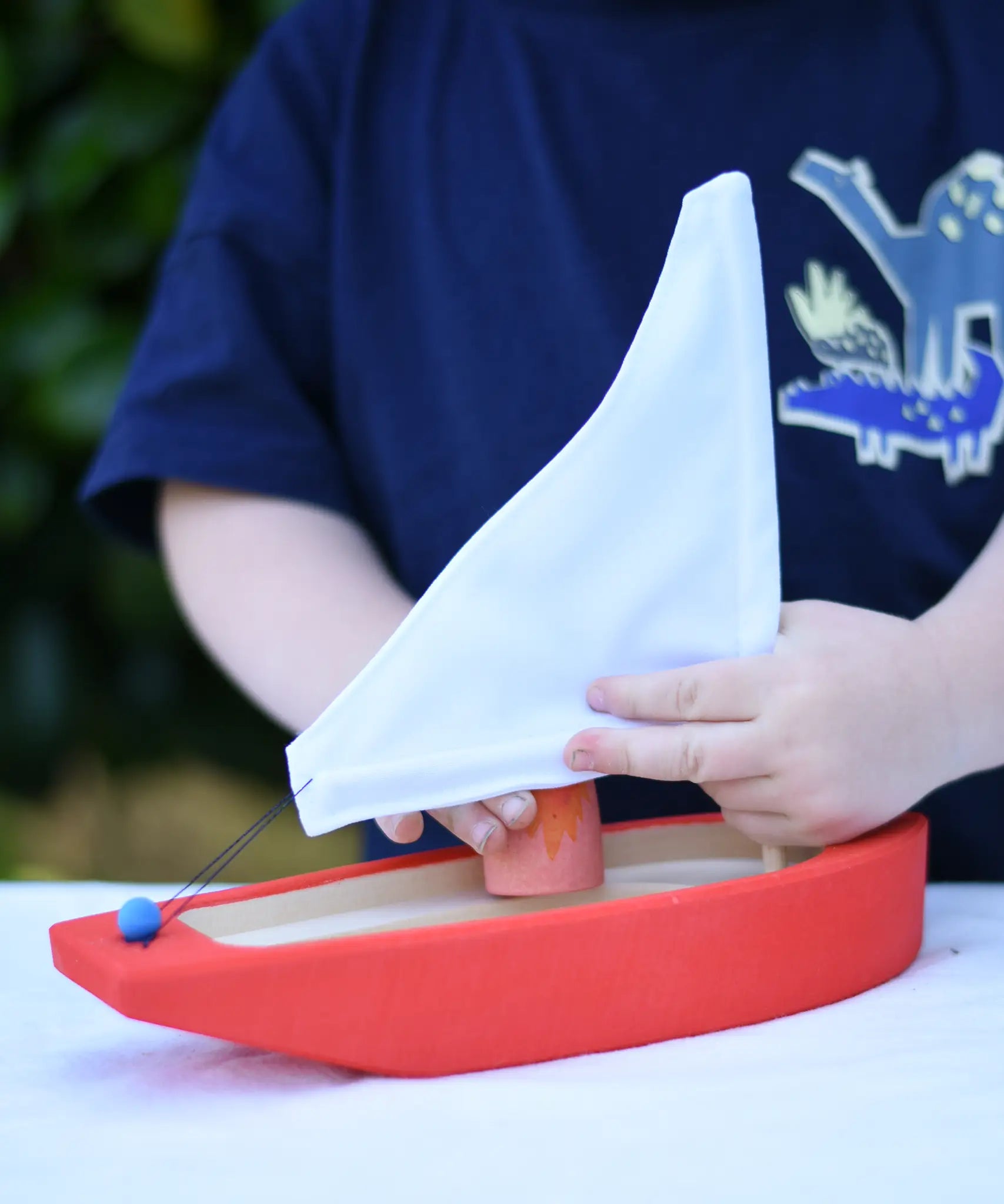 Child placing a Grapat Nin into the  Glückskäfer wooden sailing ship in red.