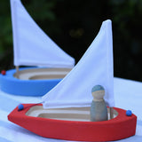  Glückskäfer wooden sailing ship in red with a blue Grapat Nin placed inside with a blue boat in the background.