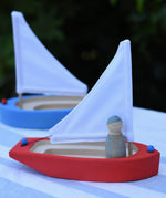  Glückskäfer wooden sailing ship in red with a blue Grapat Nin placed inside with a blue boat in the background.