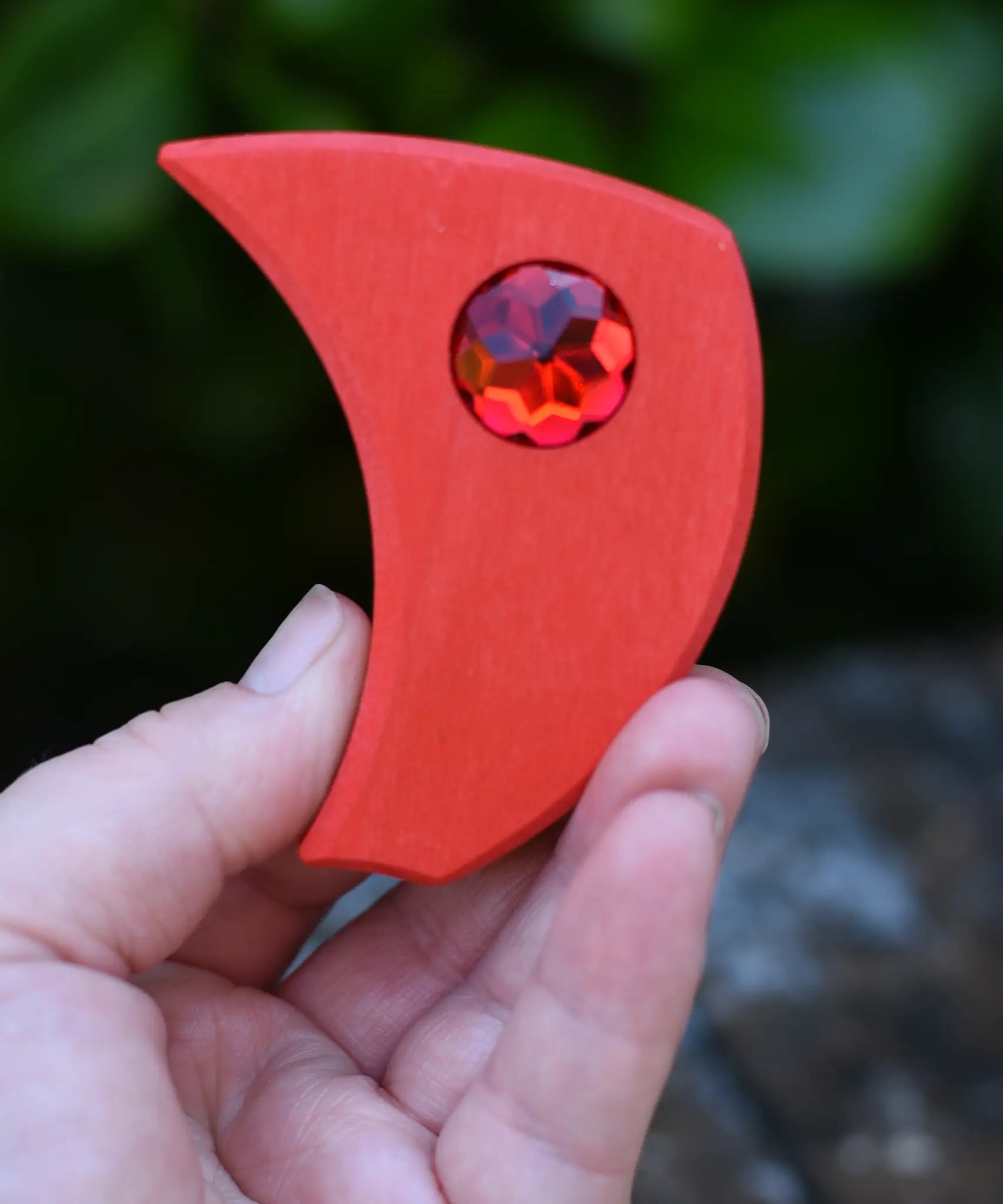 Red pieces from the Glückskäfer sparkling swirl wooden spinning toy in an adult's hand.