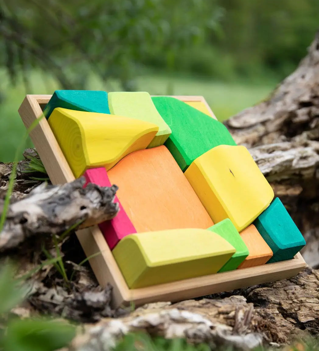 Glückskäfer Summer wooden play blocks. 11 colourful blocks in a wooden storage tray leaning against a log.