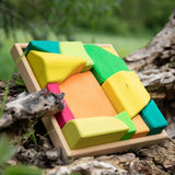 Glückskäfer Summer wooden play blocks. 11 colourful blocks in a wooden storage tray leaning against a log.