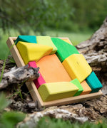 Glückskäfer Summer wooden play blocks. 11 colourful blocks in a wooden storage tray leaning against a log.