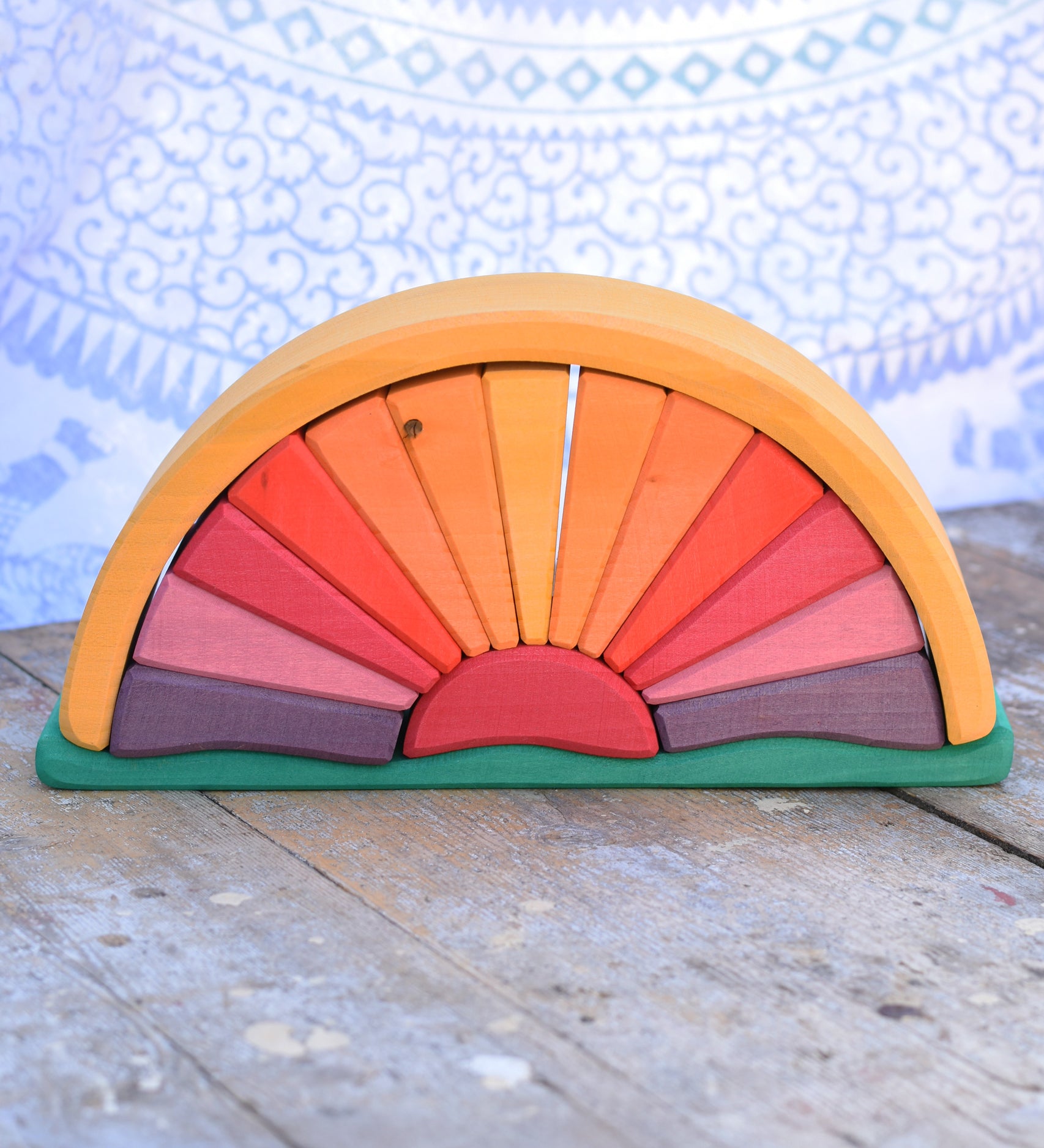 A Glückskäfer Yellow Sunray Arch placed on a wooden surface in front of a patterned cloth. 