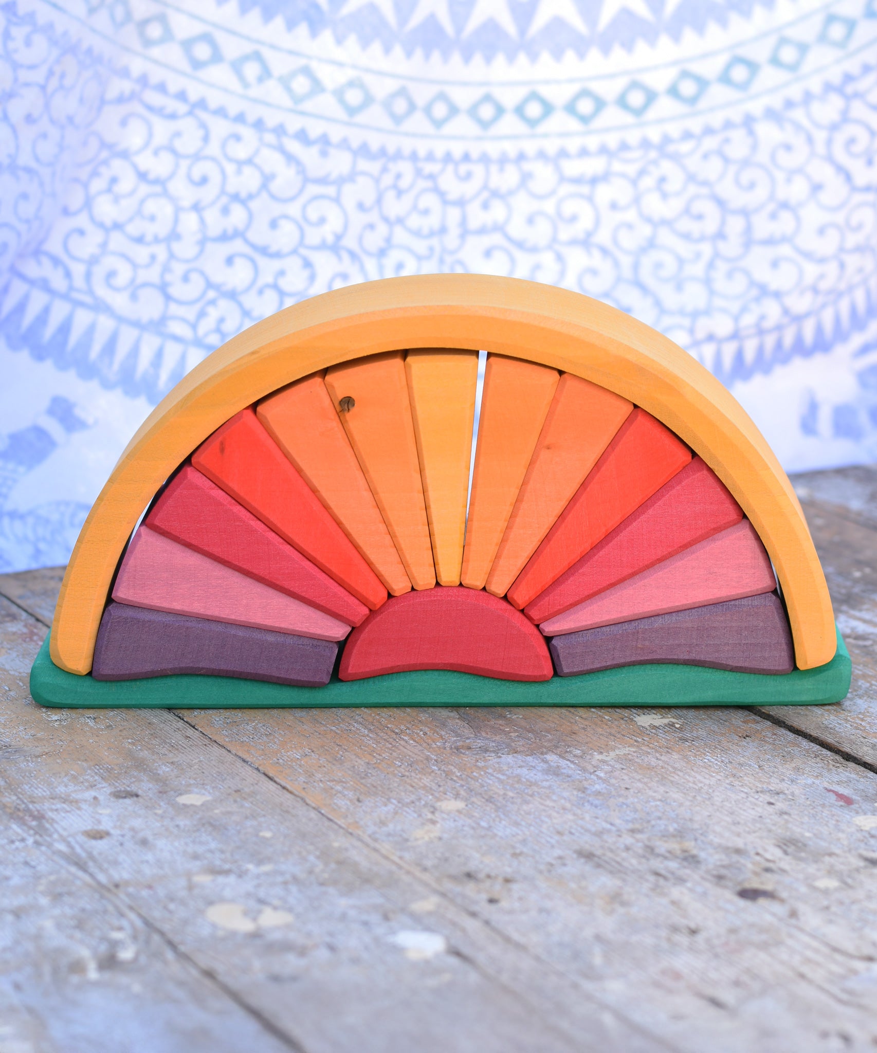 A Glückskäfer Yellow Sunray Arch placed on a wooden surface in front of a patterned cloth. 