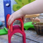 A child's hand placing a red coloured house shaped piece from the Glucksakfer castle set on a larger house shaped piece. 
