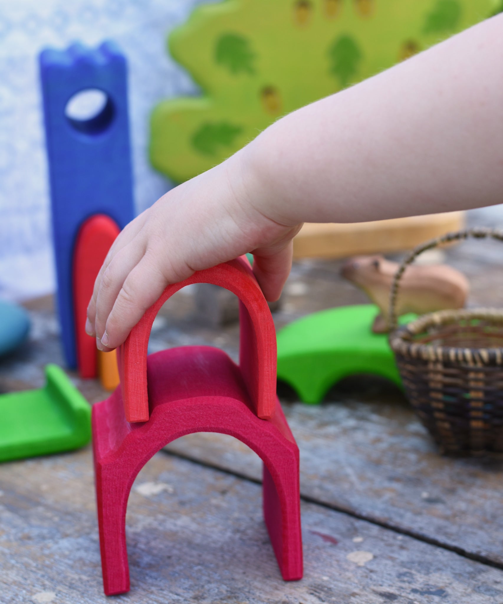 A child's hand placing a red coloured house shaped piece from the Glucksakfer castle set on a larger house shaped piece. 